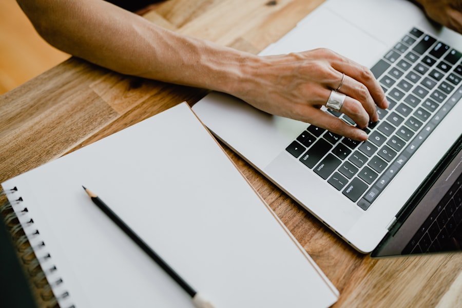 Personne tapant sur un clavier d'ordinateur portable, avec un carnet de notes à côté